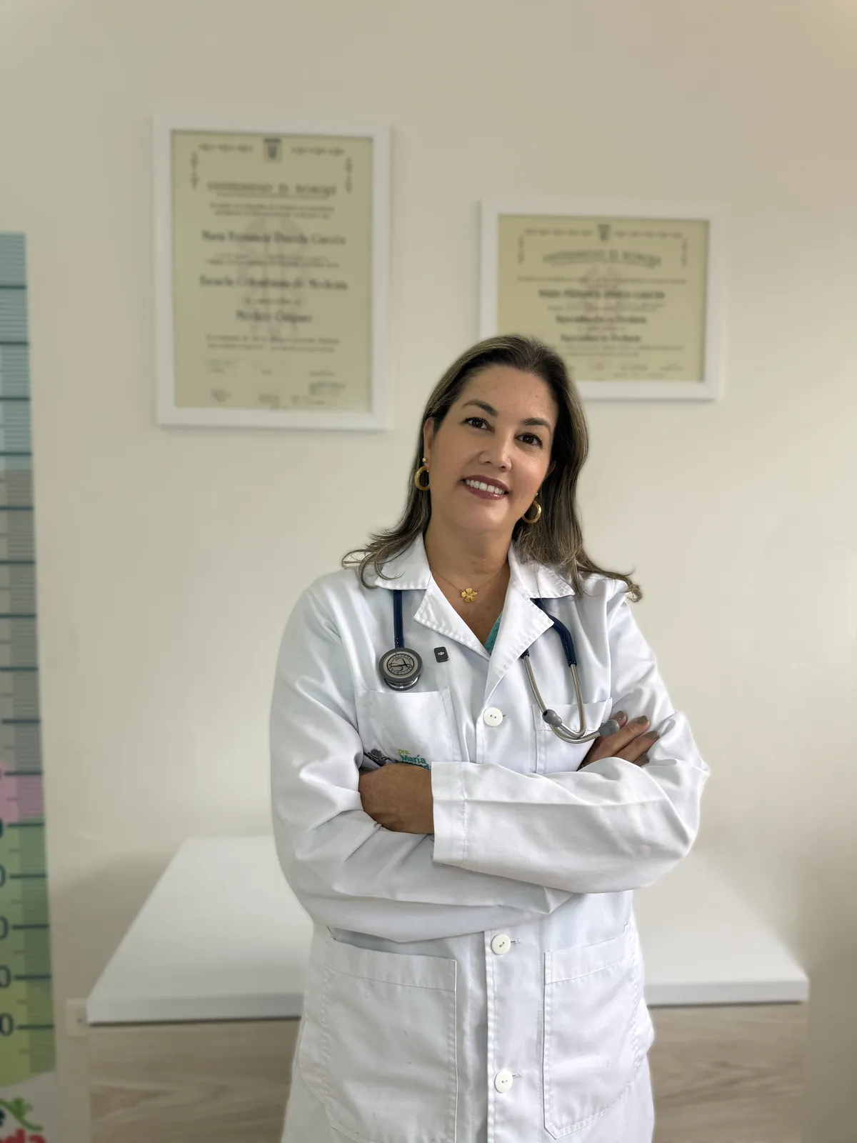 La Dra. María Fernanda Pineda con bata blanca y estetoscopio junto a sus diplomas
